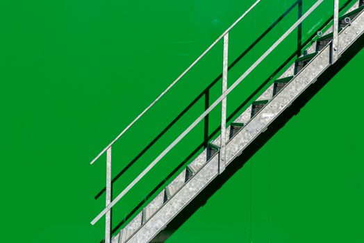 Simple metal staircase contrasting with a vivid green wall in outdoor setting.