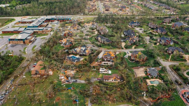 Aerial view of tornado impact on small settlement cottages with destroyed roofs windthrown trees and bent electricity transmission lines