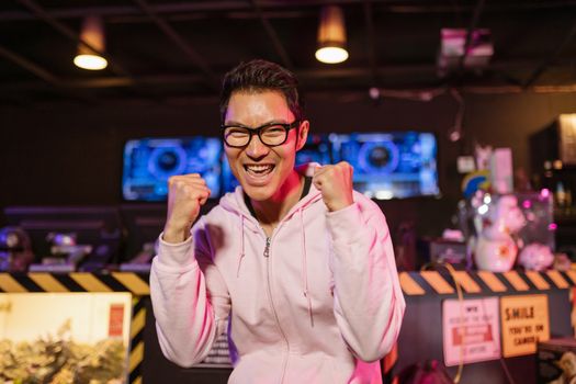 Excited gamer in hoodie celebrates a win indoors with a cheerful smile.