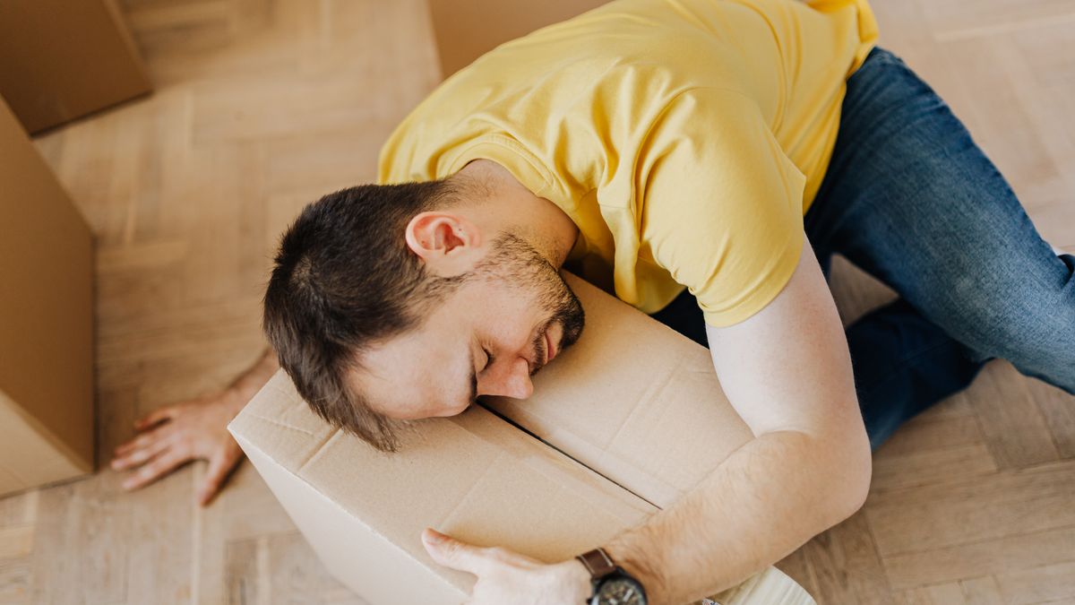 High angle of fatigued male in casual wear sleeping on floor with cardboard box after packing belongings before moving out