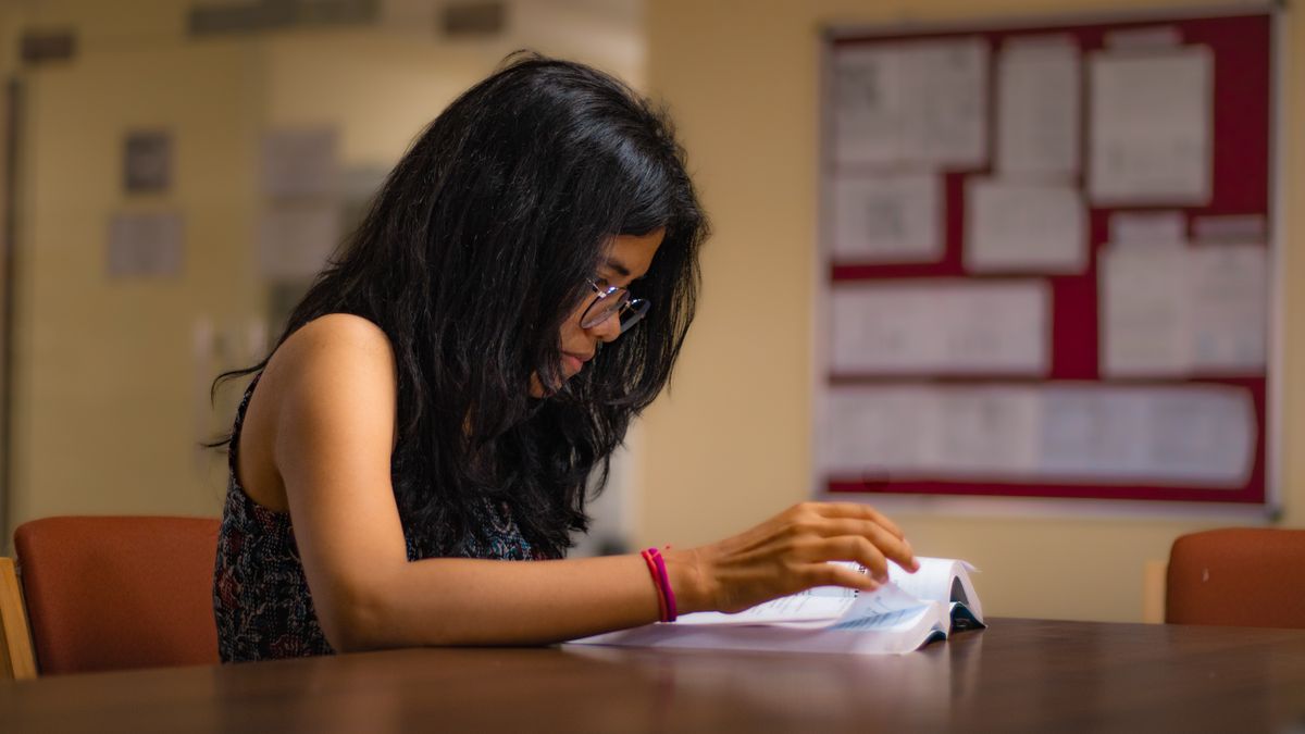Focused young woman reading a textbook at a university library desk in New Delhi.