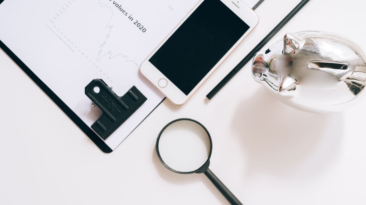 A flat lay of financial documents with a smartphone, magnifying glass, and piggy bank.