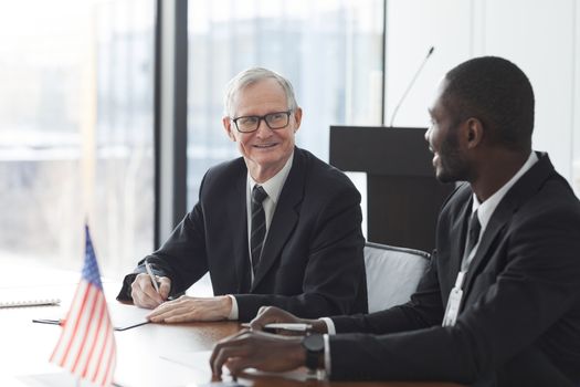 Two business professionals discussing and signing documents at a meeting with an American flag on the table.