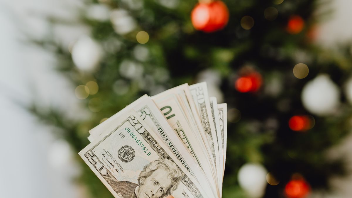 A close-up of a hand holding dollar bills with a blurred Christmas tree in the background.