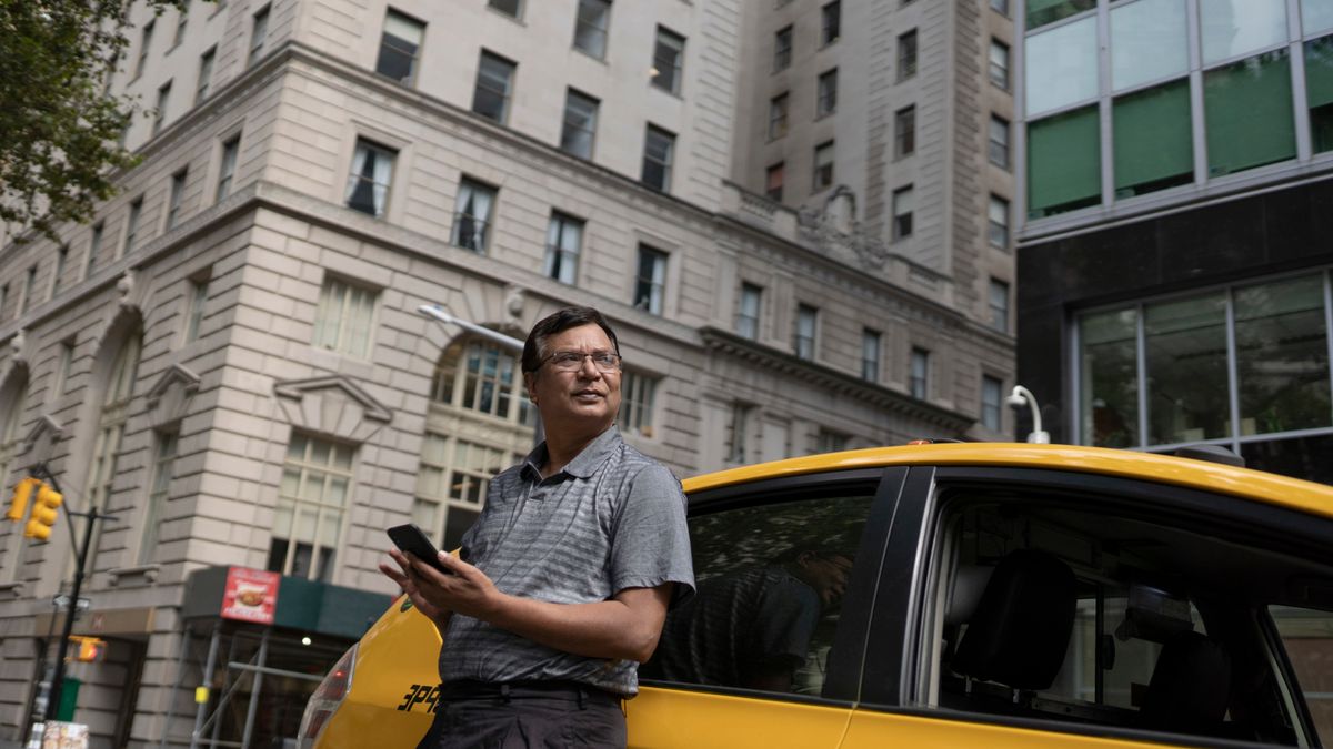 Low angle of serious ethnic male scrolling mobile phone while leaning on yellow car in downtown