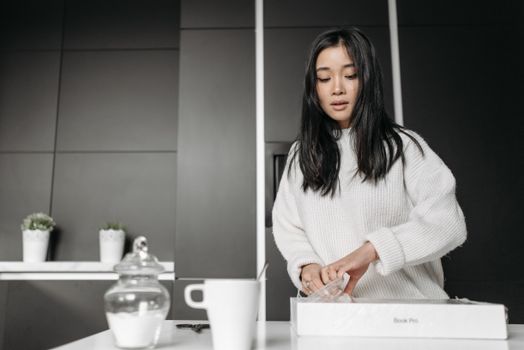 Young woman opening a box in a contemporary kitchen, surrounded by modern decor.