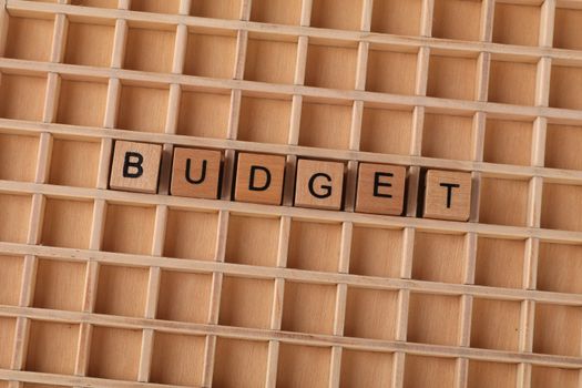 Wooden Scrabble tiles spelling 'budget' on a textured wooden grid, symbolizing financial planning.