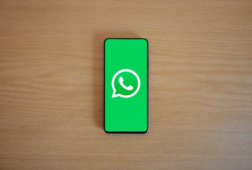 Top view of smartphone displaying WhatsApp logo on a wooden background, representing technology and communication.