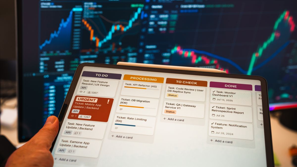 Tablet with business task management app in front of stock chart monitors.