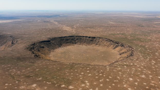 Aerial photograph of a vast, barren meteor crater in an arid landscape, showcasing nature's raw terrain.