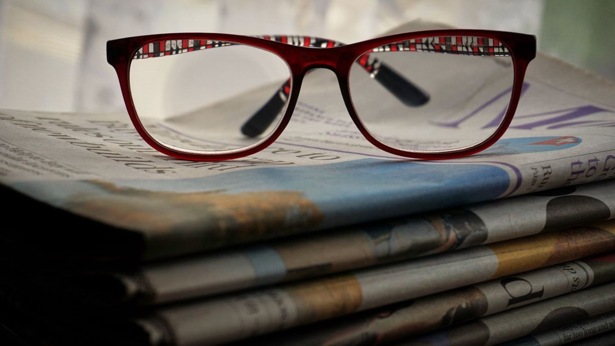 Close-up of red glasses resting on stacked newspapers, emphasizing reading and vision.