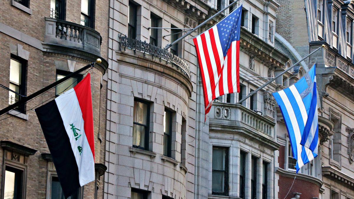 Three national flags displayed on historical city buildings in daytime.