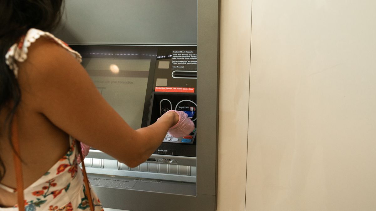 Woman using an ATM machine while wearing protective gloves indoors.
