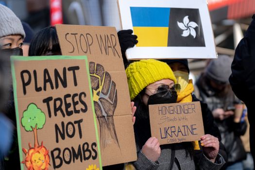 A diverse group in New York City protests for peace with signs supporting Ukraine and Hong Kong.