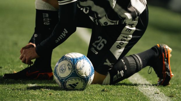 Soccer player tying shoelace before game on a sunny field. Athletic preparation for competition.