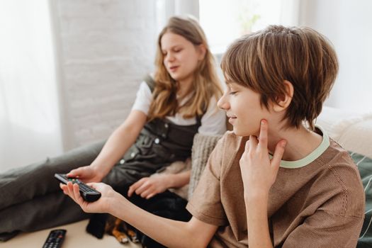 Two siblings sitting comfortably on a sofa, enjoying television together indoors.