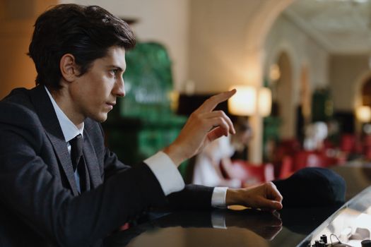 Elegant man in a suit making a gesture at a luxurious bar in a sophisticated setting.
