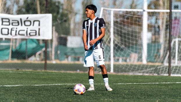 A young soccer player in a striped jersey focuses on the field, ready to kick the ball during the game.