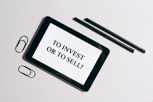 Flat lay of tablet with investment decision text, surrounded by stationery on a white table.