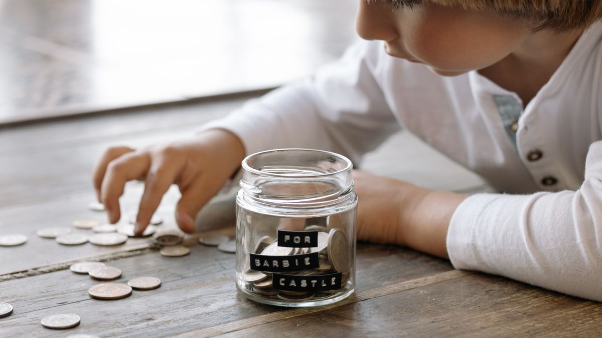 A young child collects coins in a jar labeled 'For Barbie Castle', symbolizing saving and dreams.