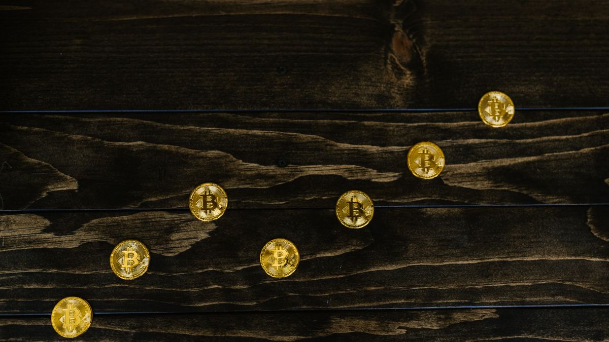 Gold-colored bitcoins arranged diagonally on a dark wooden surface.