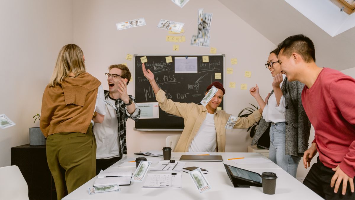 A joyful office team celebrates with money in the air, symbolizing success and teamwork.
