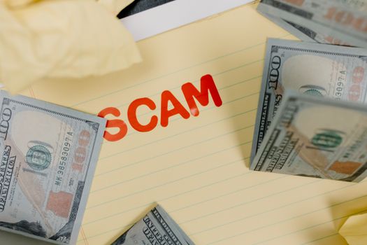 Conceptual image of financial scam with US dollars on yellow paper and word 'scam' visible.
