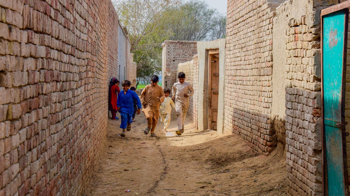 Group of boys walking through a narrow alley between brick walls in Jalalpur Pirwala, Punjab, Pakistan.