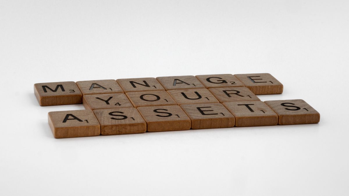 Wooden Scrabble tiles spelling 'Manage Your Assets' on a white background.