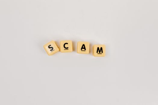 Four Scrabble tiles forming the word 'SCAM' on a neutral background, highlighting concepts like deceit.