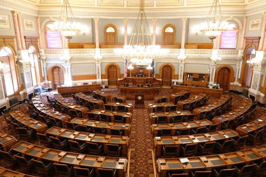 Wide view of an ornate legislative chamber with empty seats and chandeliers.