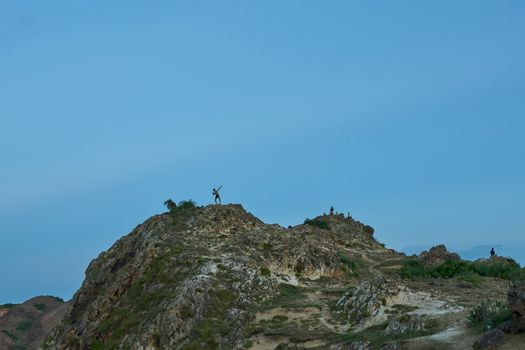An adventurous person stands atop a rocky hill in Quy Nhon, Vietnam, under a clear blue sky.