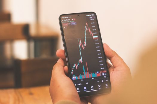 Person holding smartphone with stock market graph, portraying financial trends.