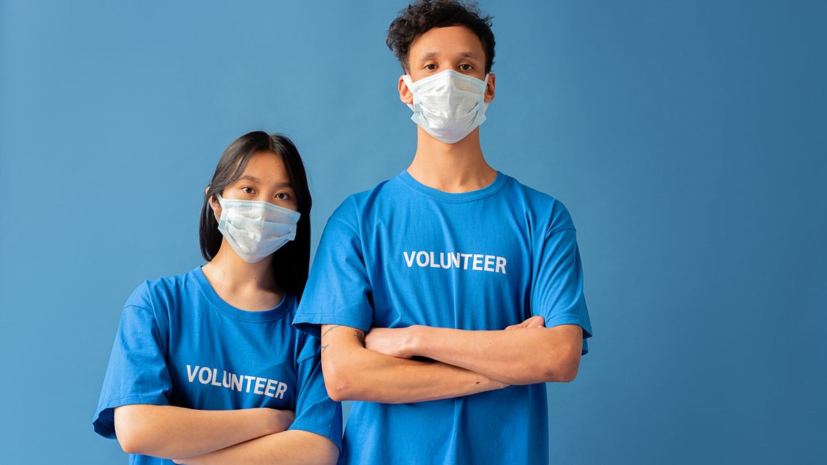 Two masked volunteers standing with arms crossed against a blue backdrop.