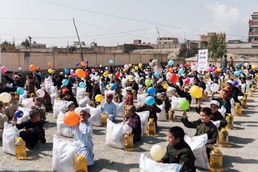 Children gather with balloons and supplies during a daytime event in Afghanistan.