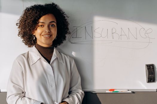 African American woman smiling in office setting with a whiteboard displaying 'Insurance'.