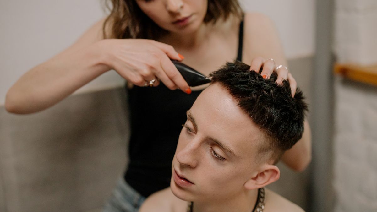 A woman gives a haircut to a young man at home, focusing on personal grooming and DIY skills.