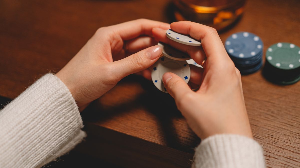A person in a white sweater playing with poker chips on a wooden table.