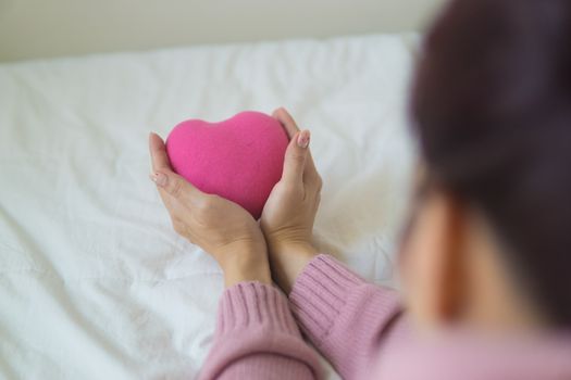 From above of unrecognizable female in sweater sitting on white blanket with pink heart shaped exercise ball in light room