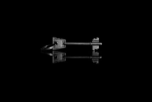 A vintage skeleton key with a reflection on a glossy black surface, showcasing a monochromatic minimalist style.