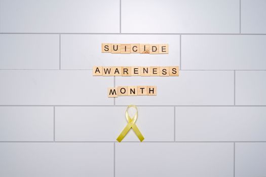 Scrabble tiles and yellow ribbon promoting Suicide Awareness Month on a tile background.