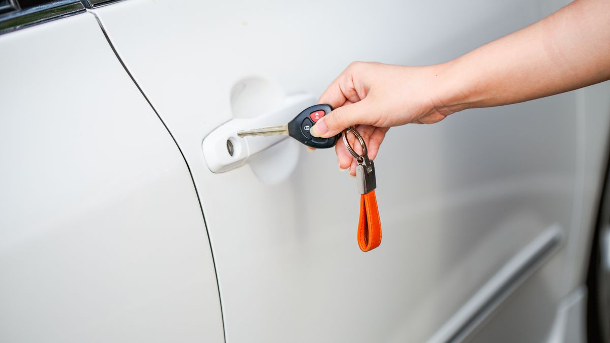Close-up of a hand unlocking a white car door with a metal key and key fob.