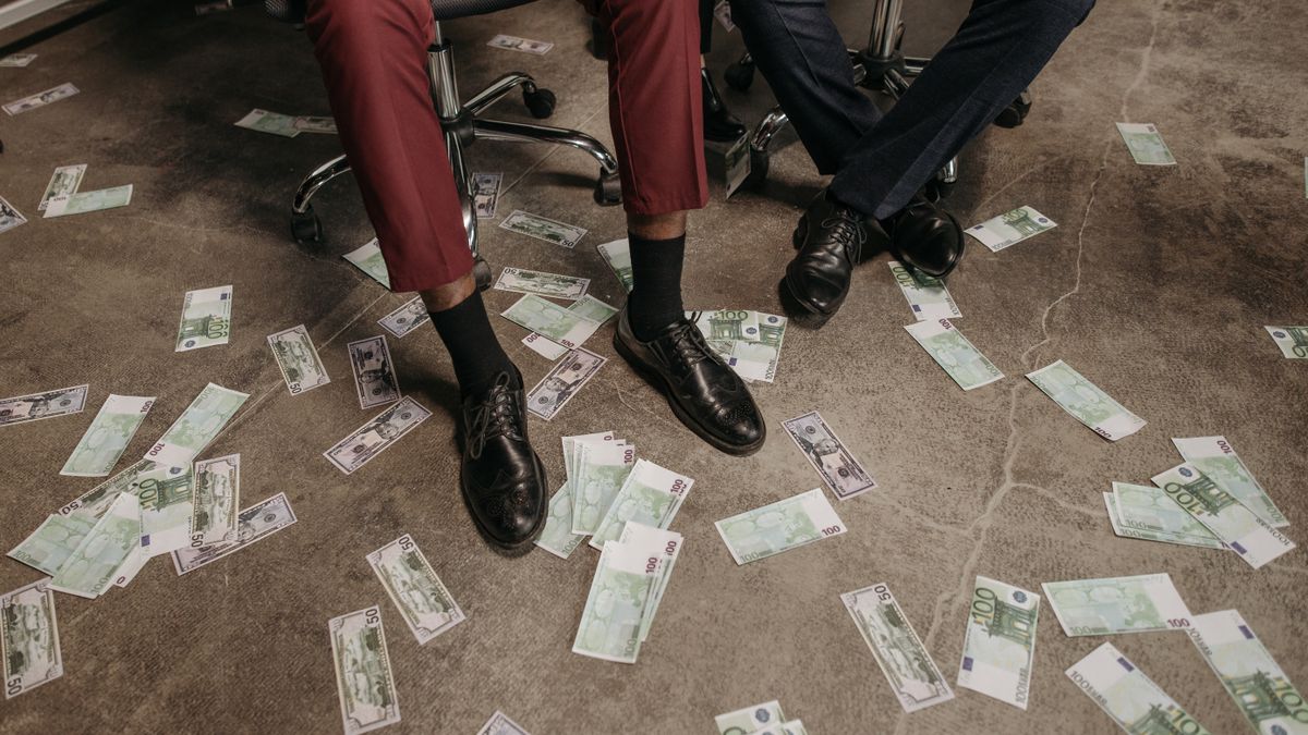 Two people in an office with euro banknotes scattered on the floor, showcasing a financial theme.